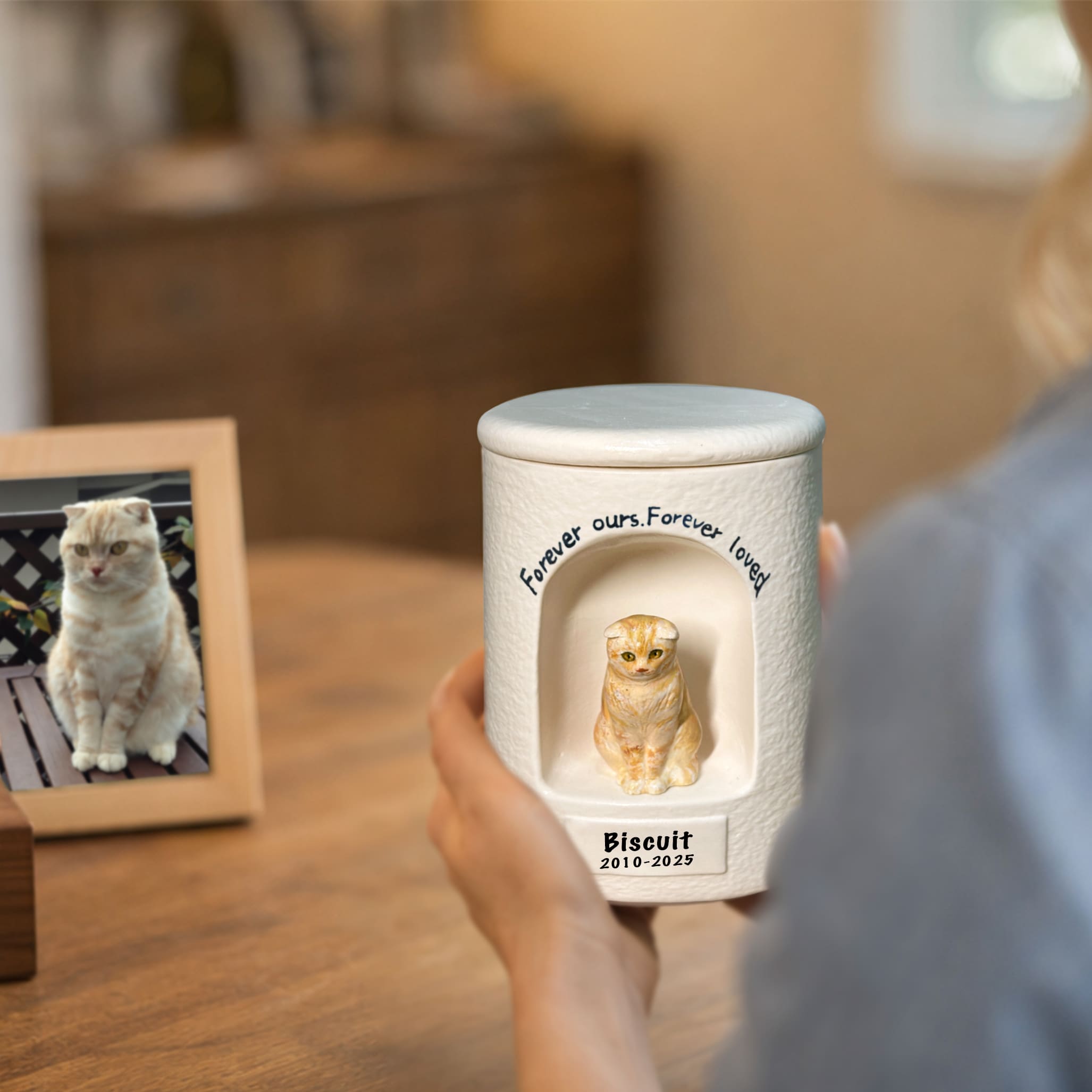 White cat memorial urn with gold figurine and engraved dates, held in hands