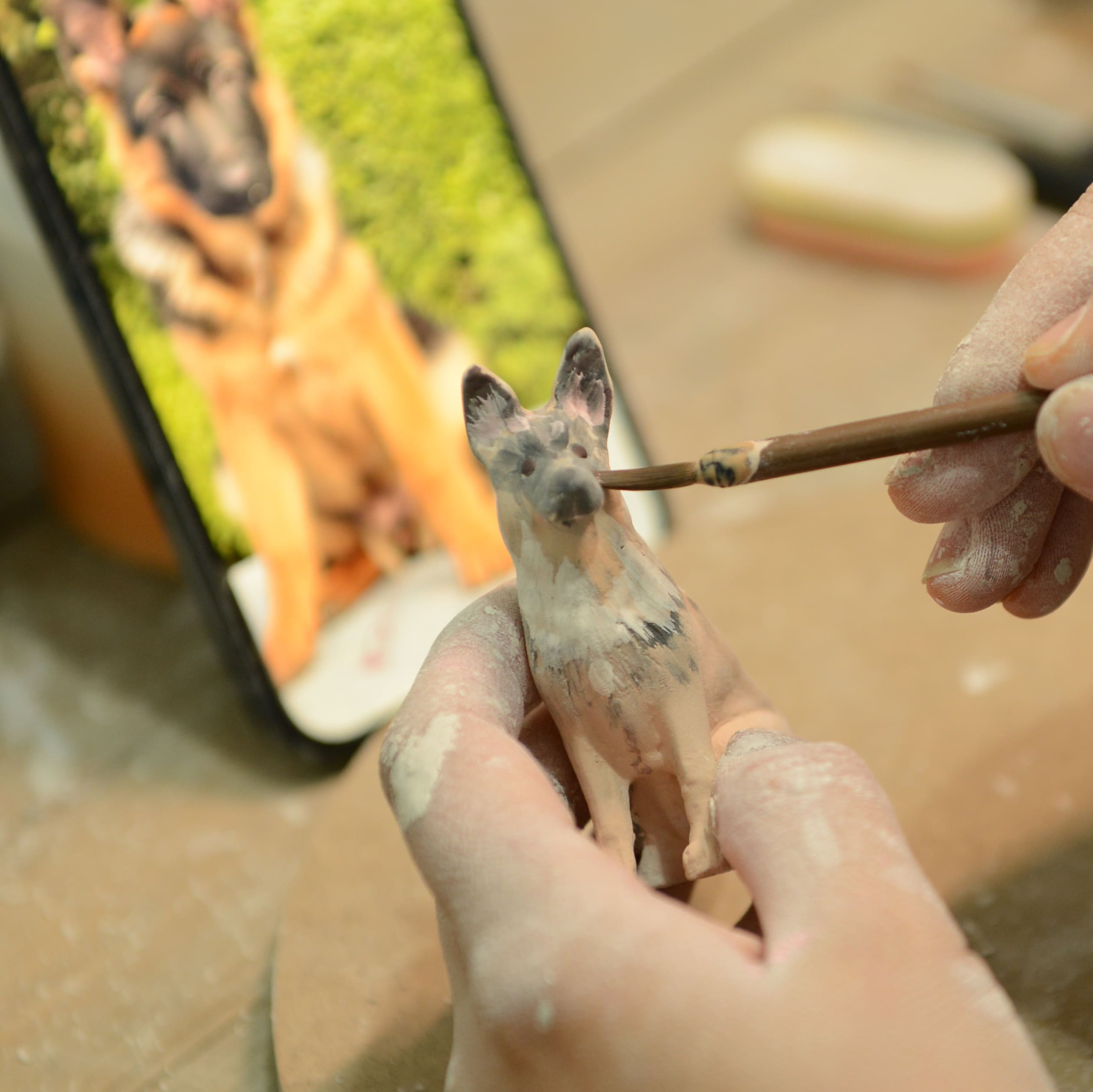 Ceramic dog figurine being painted, light gray dog detail with paintbrush