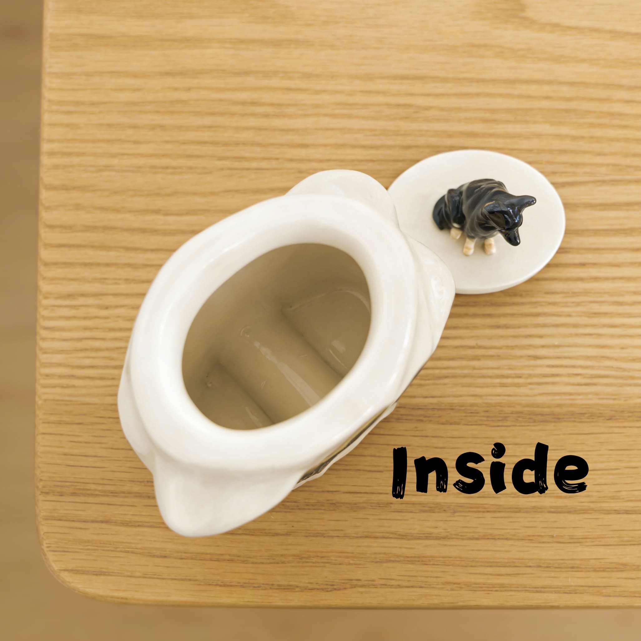 Open cream ceramic pet urn base with black dog figurine lid showing hollow interior