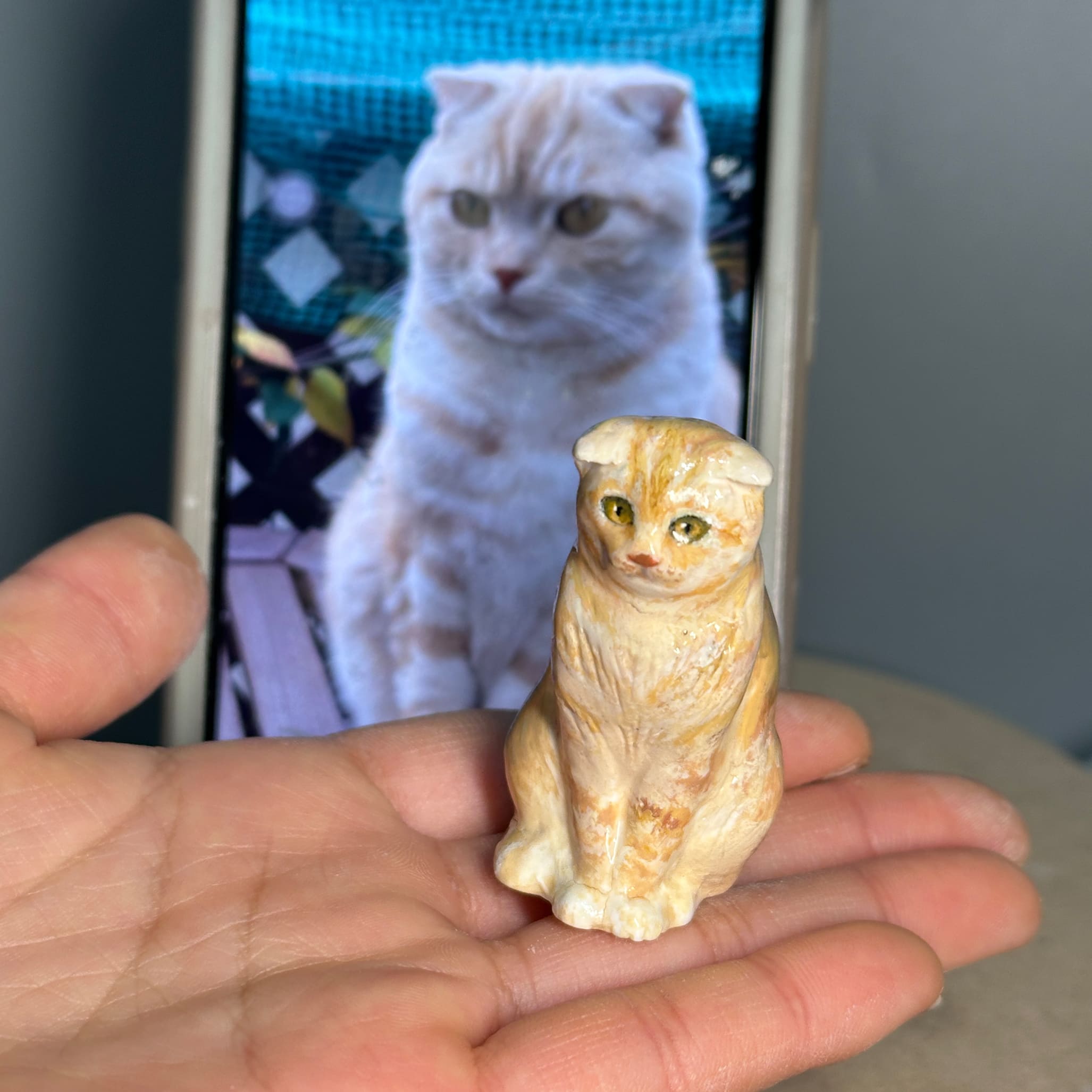 Sculpted cat figurine held in hands, cream color with painted facial details