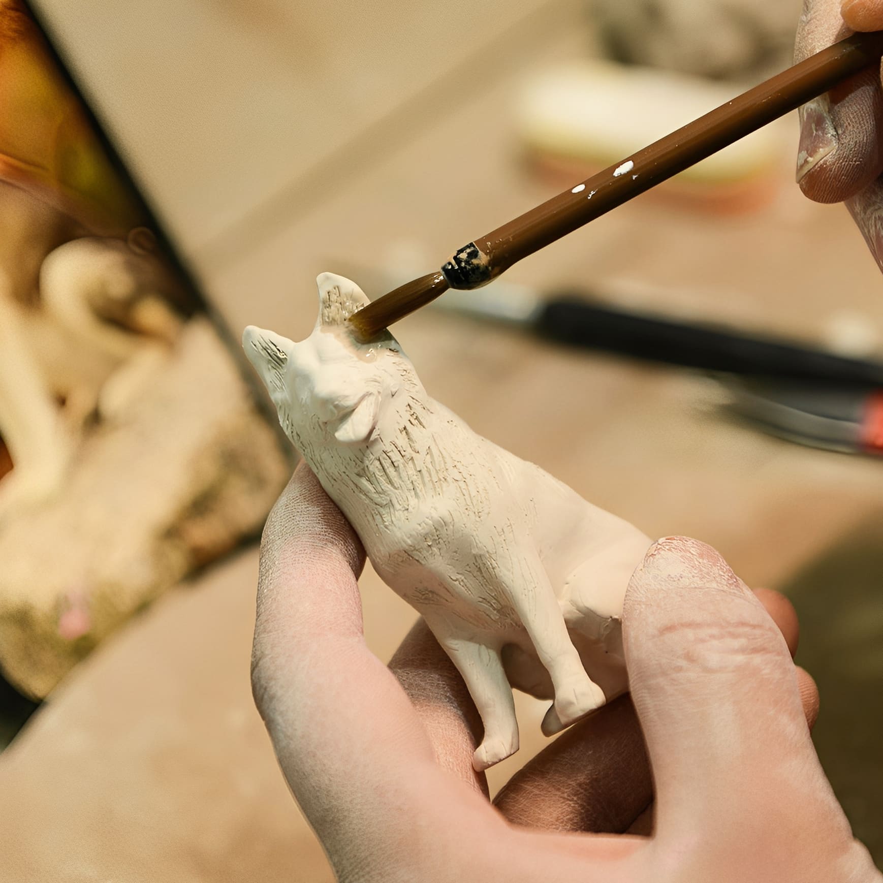 Ceramic dog figurine being painted with brush over sculpted surface