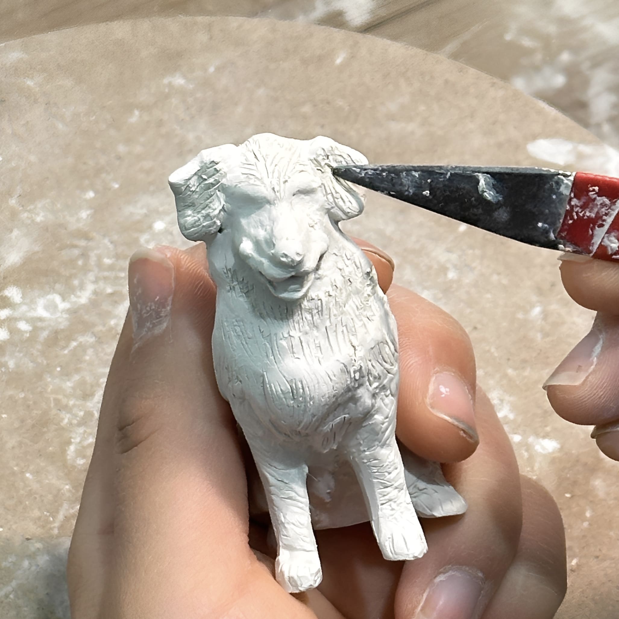 Custom dog urn figurine, white dog sculpture being shaped in a hand