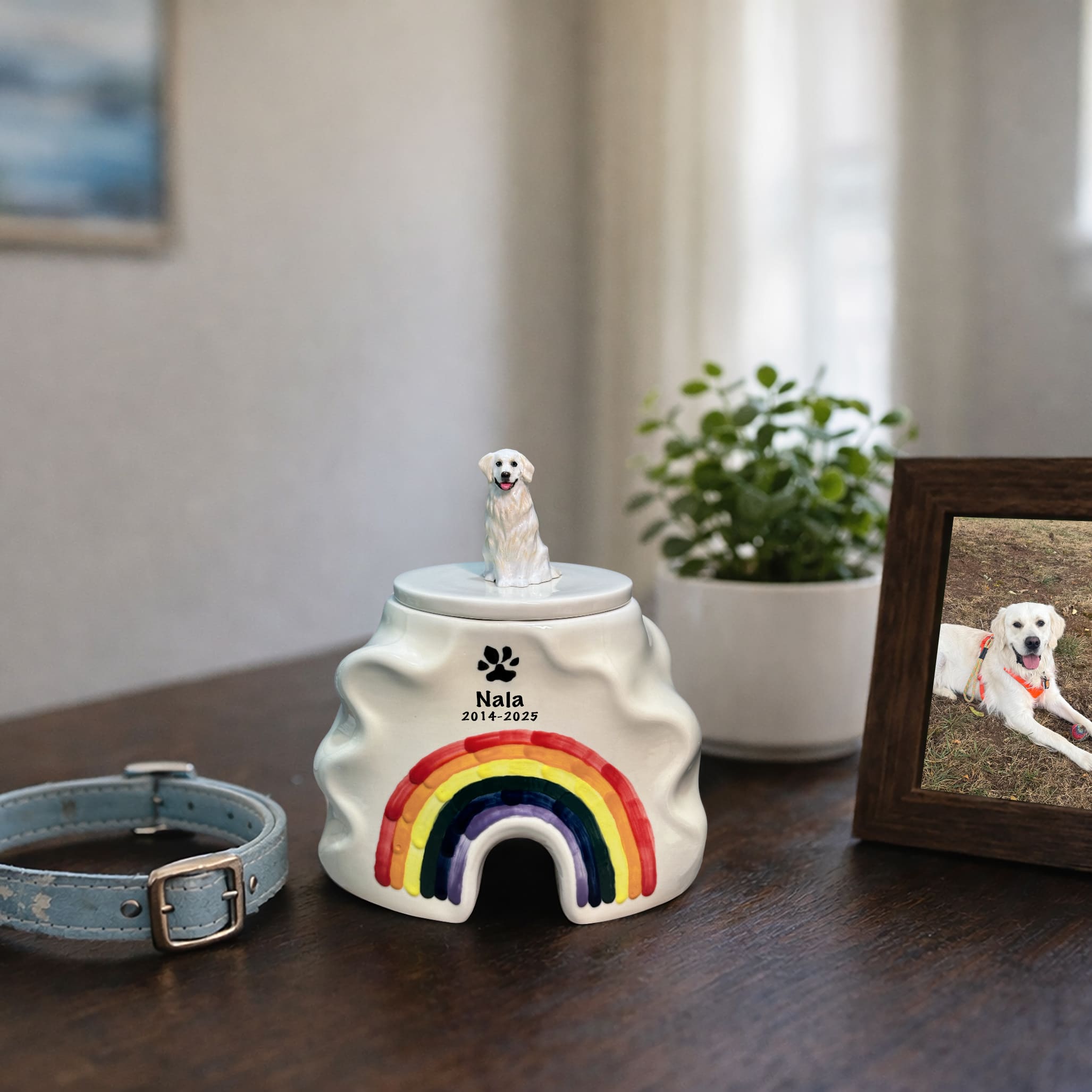 Ceramic dog urn on tabletop with rainbow arch and seated white dog on lid