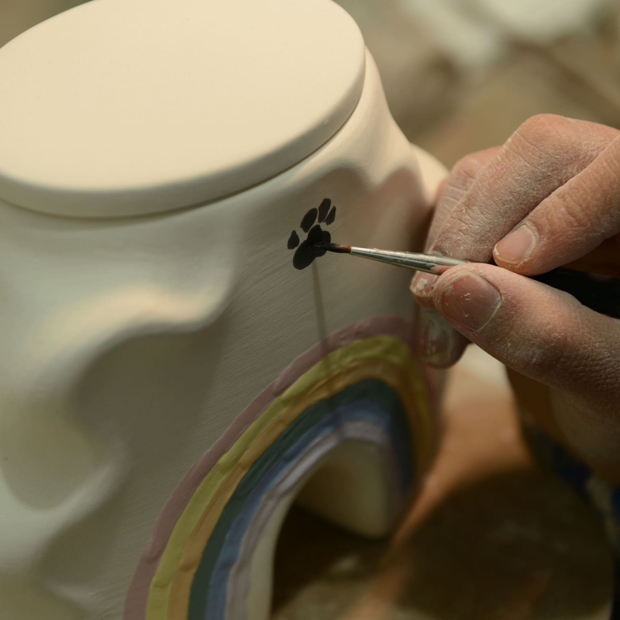 Hand filling a rainbow bridge ceramic dog memorial urn lid opening with a small tool